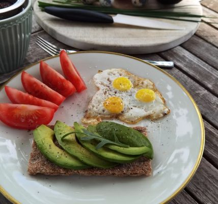 A vibrant outdoor breakfast setup with avocado toast, quail eggs, tomatoes, and tea.