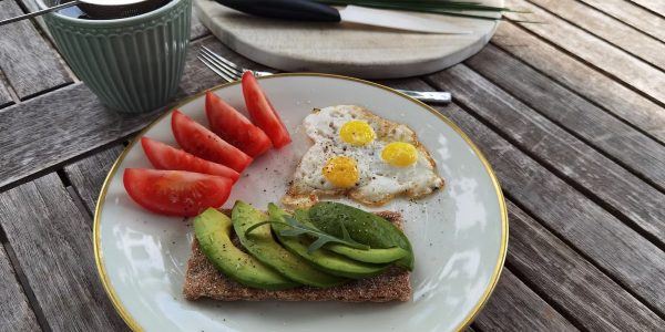 A vibrant outdoor breakfast setup with avocado toast, quail eggs, tomatoes, and tea.